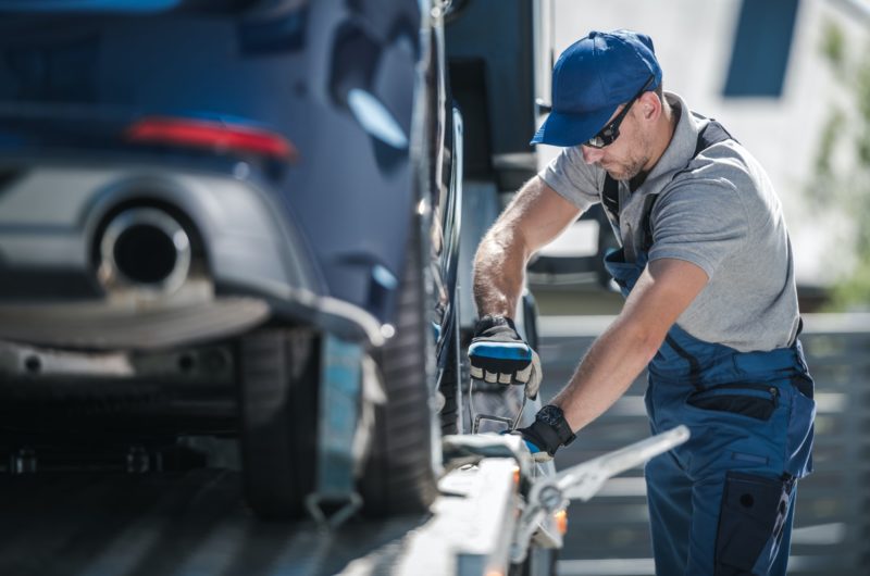 towing-company-worker-securing-vehicle-on-the-truck-platform-800x530